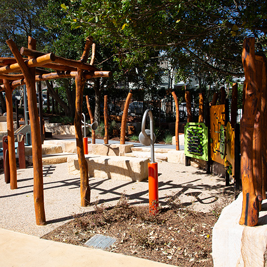 Playgournd equiptment shaped like thin brown tree branches in a playground surrounded by trees